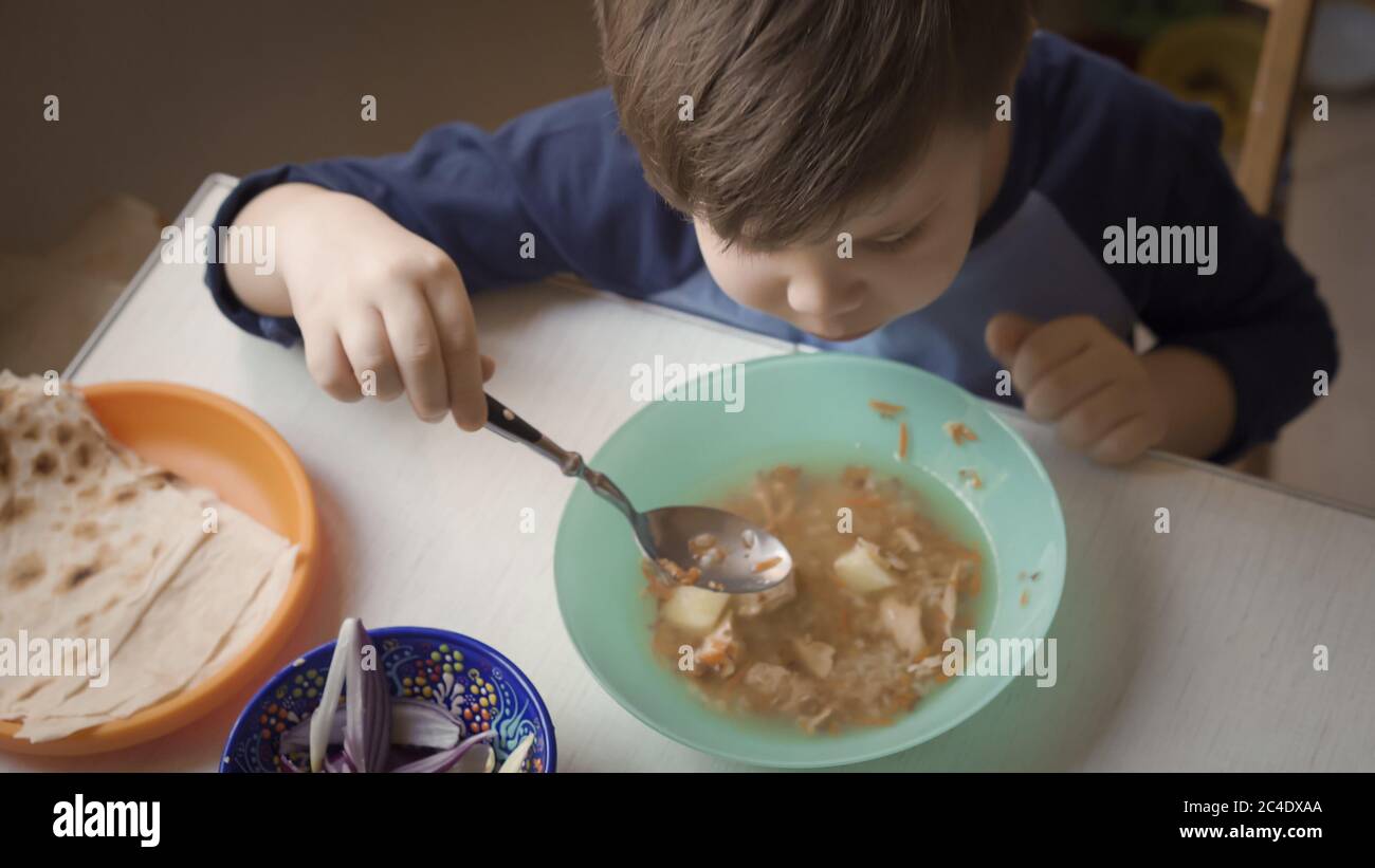 Das Kind im Vorschulalter lernt, Suppe selbst am heimischen Küchentisch zu essen. Gesundes Essen Konzept. Draufsicht Stockfoto
