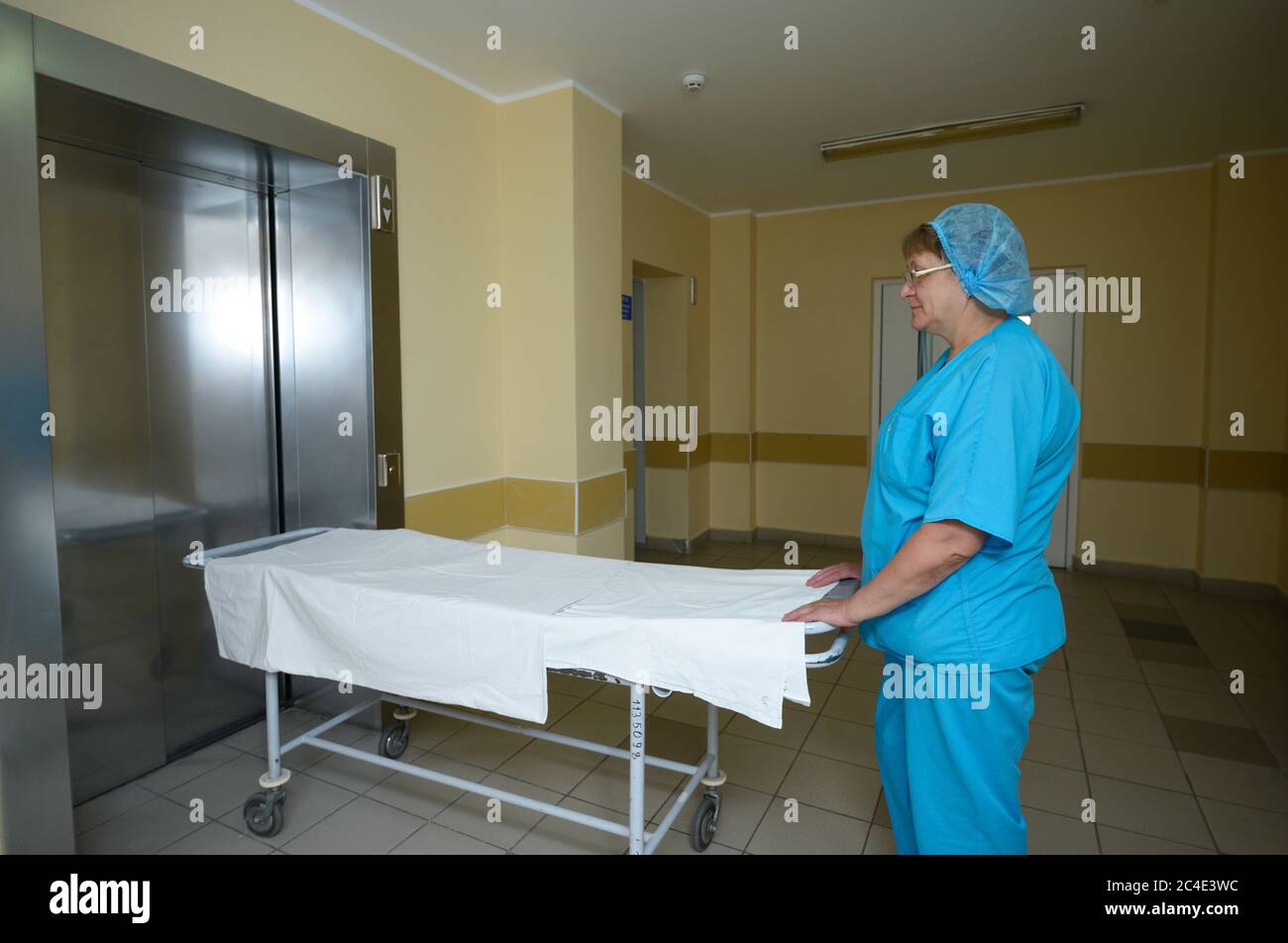 Krankenschwester in einem blauen Laborkittel, die mit einer Bahre auf dem Flur des Krankenhauses steht und auf einen Aufzug wartet Stockfoto