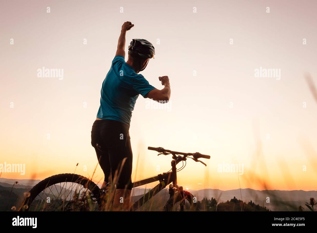 Mann Biker Mann trifft einen Sonnenuntergang auf dem Hügel. Er einen Arm aufsteigende Gruß an einem anderen erfolgreichen Tag zu Ende. Active Sport People Konzept Bild Stockfoto