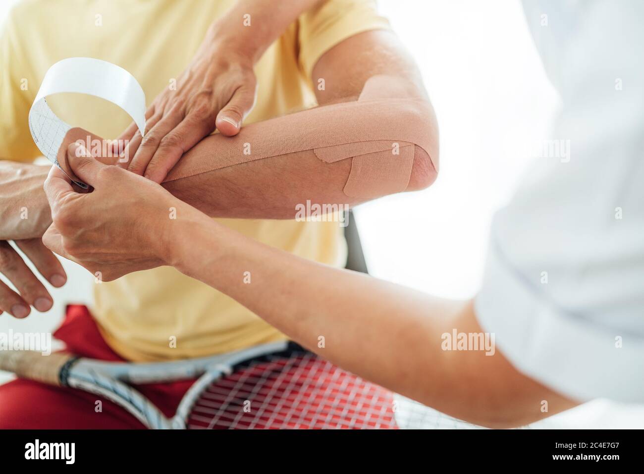 Ellenbogen des Tennisspielers mit elastischem therapeutischem oder Kinesio-Band, das von der Krankenschwester auf der orthopädischen Station angebracht wurde. Nahaufnahme. Aktiv sportlich Menschen Gesundheit reh Stockfoto
