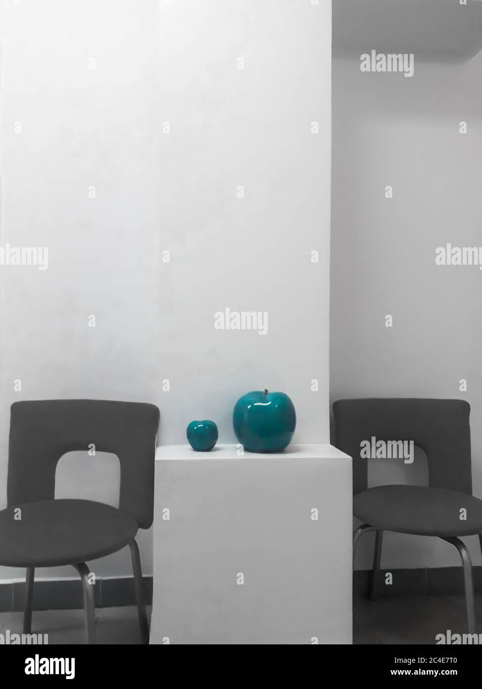 Details der Innenausstattung - eine weiße Wand, Bürostühle und zwei Keramik-Äpfel in türkisfarbener Farbe. Stockfoto