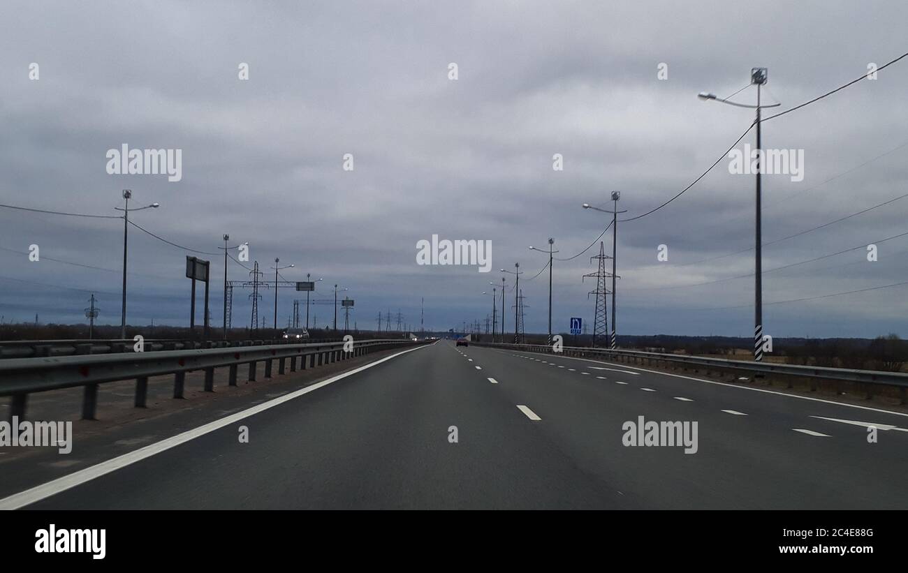 Eine Straße oder eine Autobahn, die Autobahn erstreckt sich bis zum Horizont. Blick vom Fenster des Autos. Reise, der Weg nach Hause. Kalte nördliche Natur, Sommer, grau bewölkt niedrigen Himmel. Stockfoto