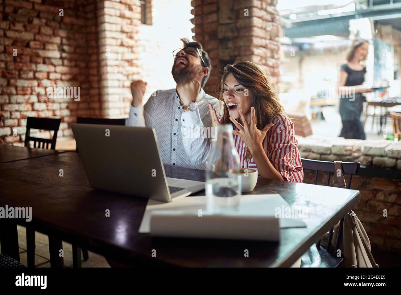 Junge kaukasische Paar Blick auf Laptop vor ihnen, Empfang gute Nachrichten, glücklich, zufrieden, Kaffee trinken im Café Stockfoto