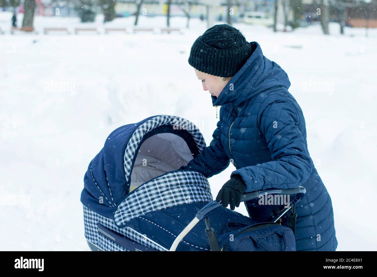 Eine junge Mutter geht mit einem Kinderwagen an einem verschneiten Wintertag Stockfoto