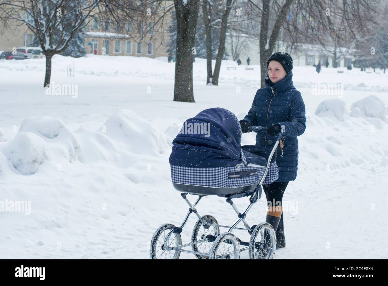 Eine junge Mutter geht mit einem Kinderwagen an einem verschneiten Wintertag Stockfoto