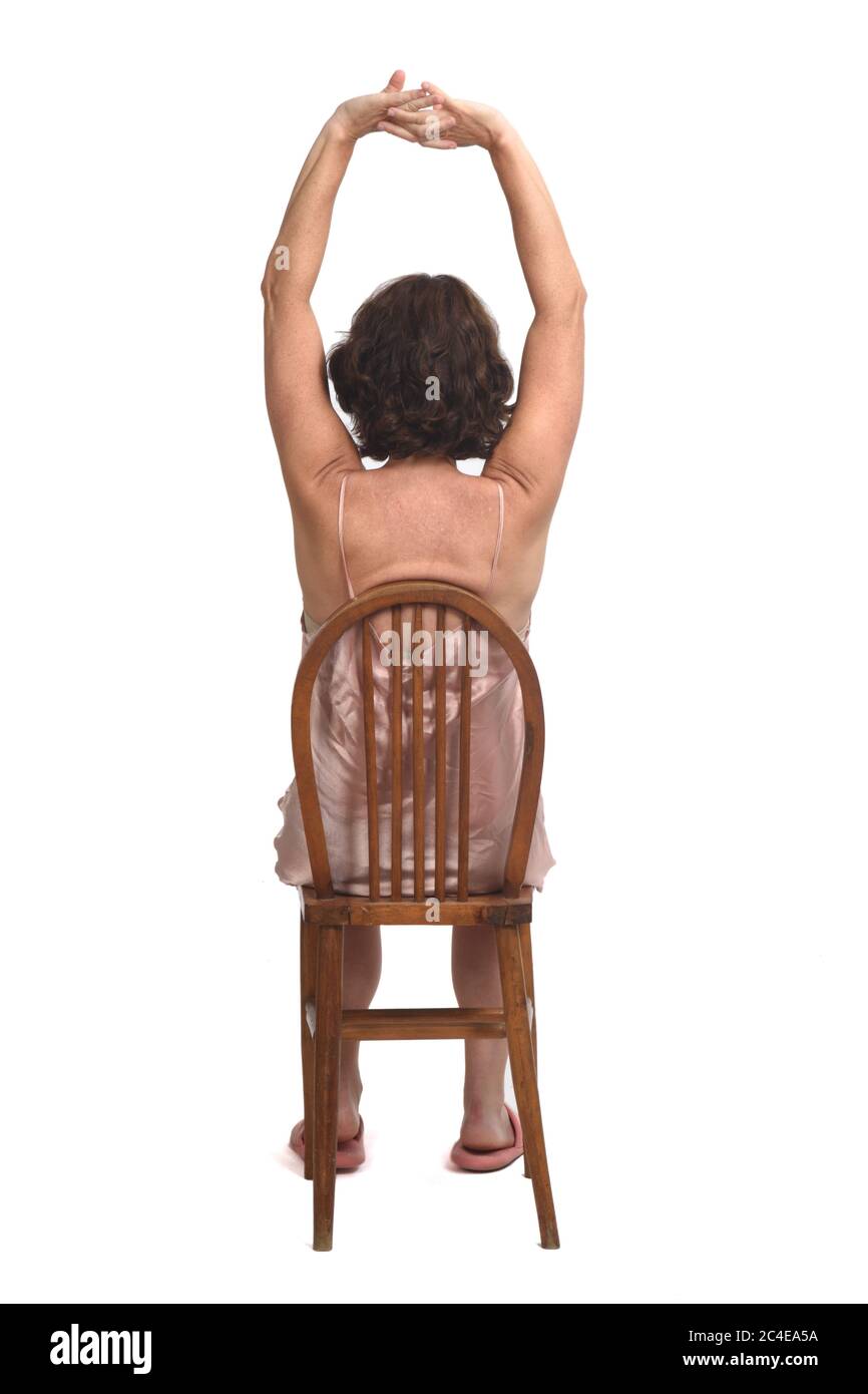 Rückansicht einer Frau, die mit Nachthemd auf weißem Hintergrund sitzt, Arme ausgestreckt; Stockfoto