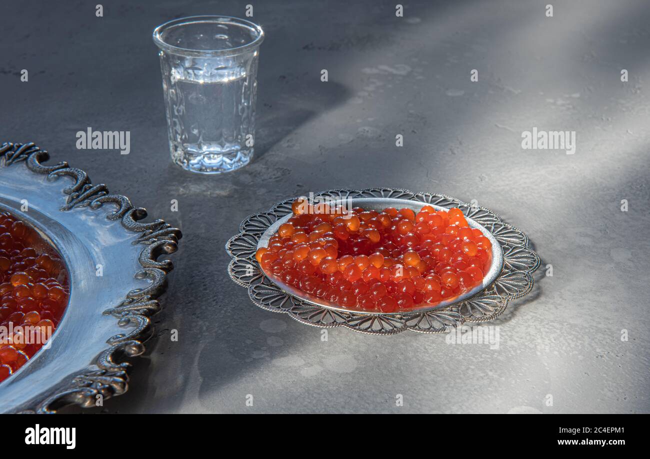 Natürlicher roter Kaviar auf silbernen Tellern auf grauem Hintergrund. Wodka Schrott auf unfokussierten Hintergrund. Selektiver Fokus. Gesunde Ernährung Konzept. Russischer Stil Stockfoto