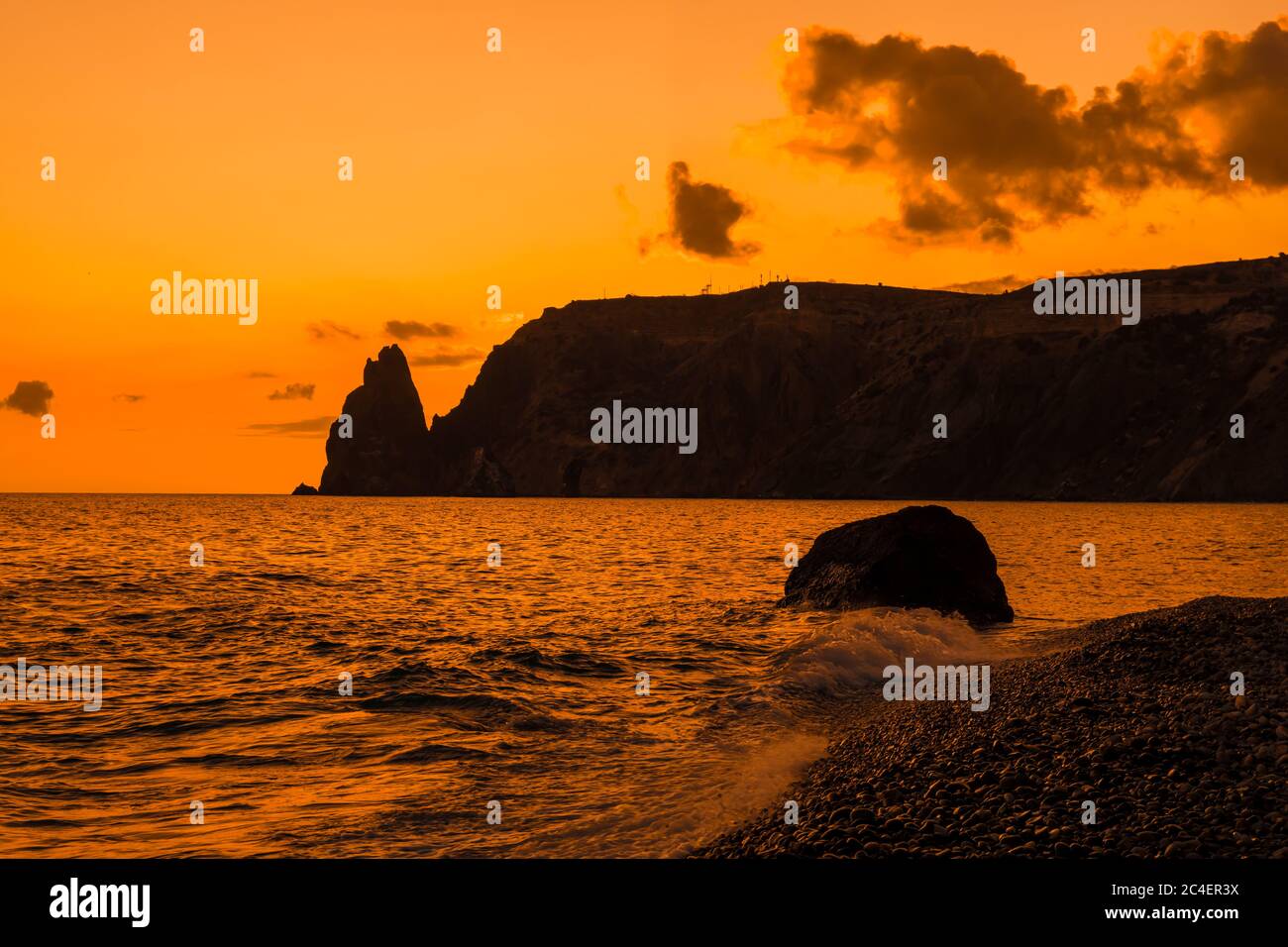 Ein rot brennender Sonnenuntergang mit dem Silhouett einer Klippe über dem Meer Stockfoto