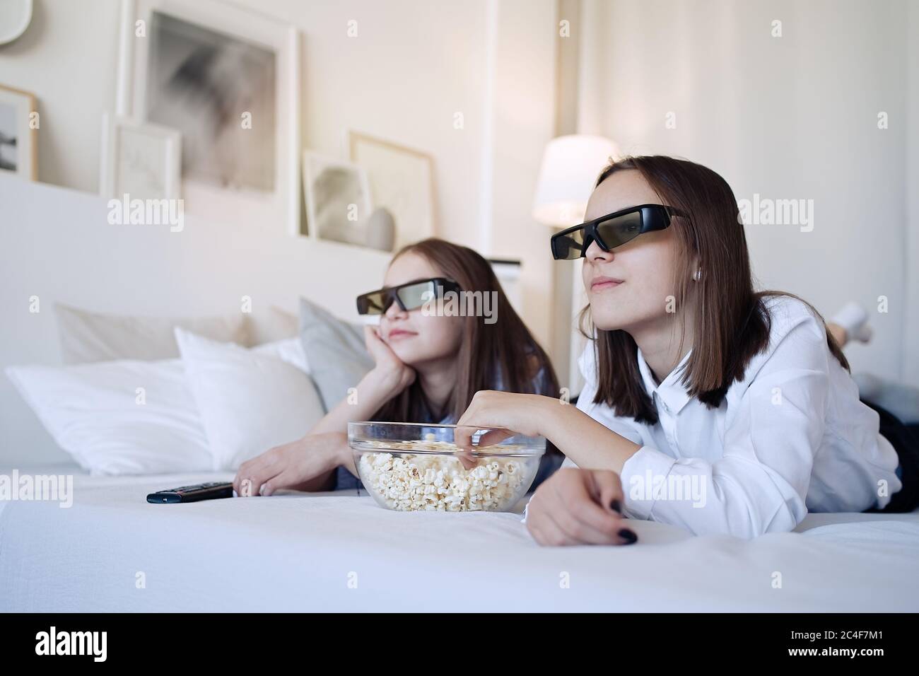 Glückliche Freunde oder Teenager-Mädchen mit 3D-Brille essen Popcorn und Film zu Hause Stockfoto