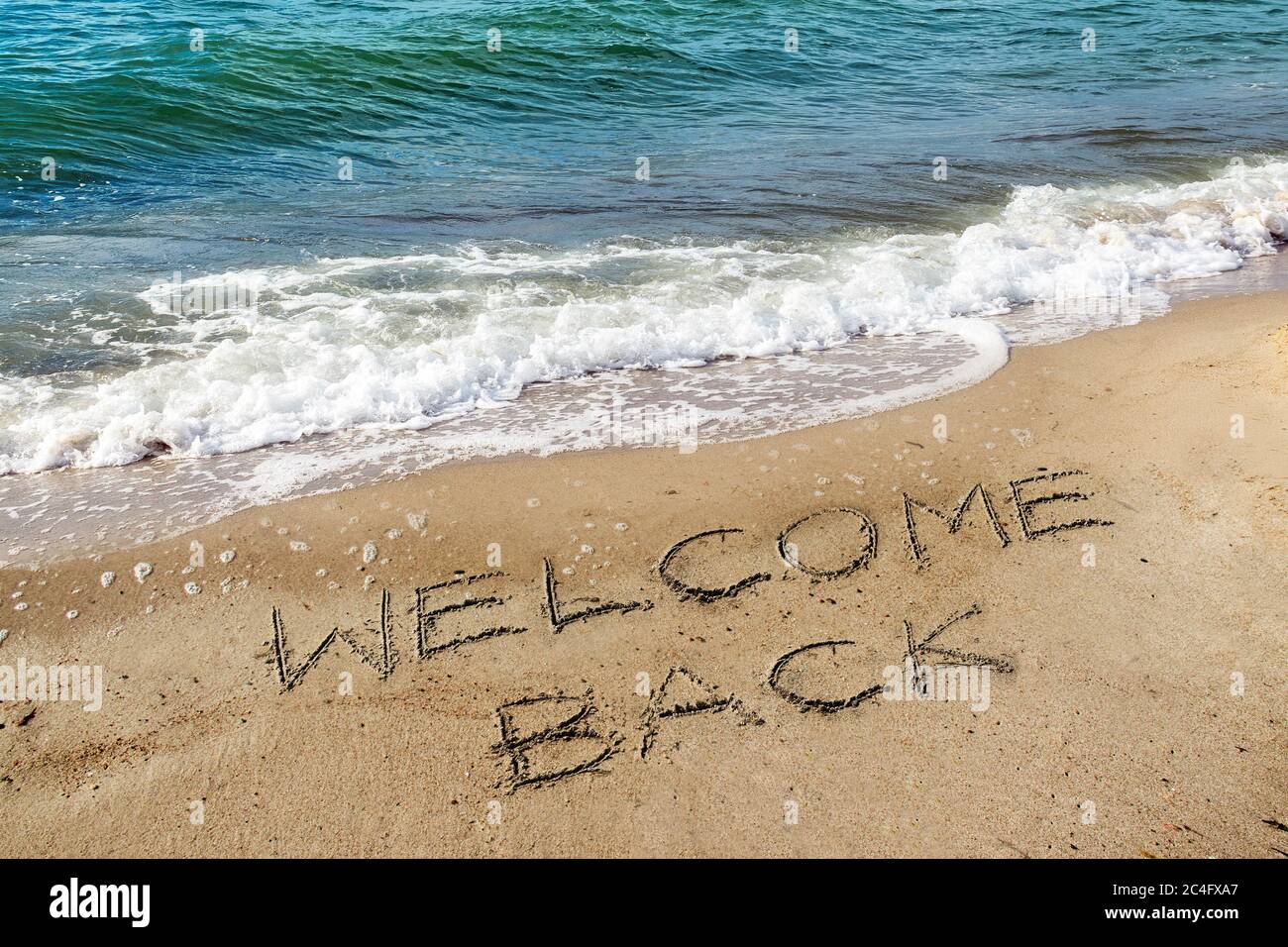 Worte Willkommen Zurück sind in den Sand am Strand in der Nähe des Wassers geschrieben, wieder nach der Coronavirus Pandemie, sind Ferien auf See wieder möglich für tou Stockfoto