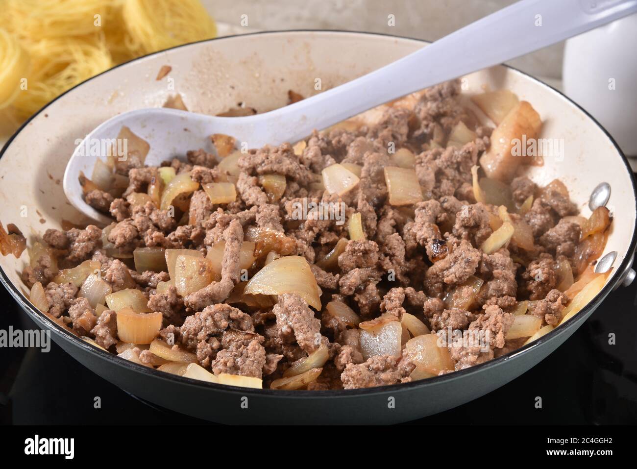 Dampfend heißes Hackfleisch und Zwiebeln in einer gusseisernen Pfanne mit Spaghetti-Nudeln im Hintergrund Stockfoto