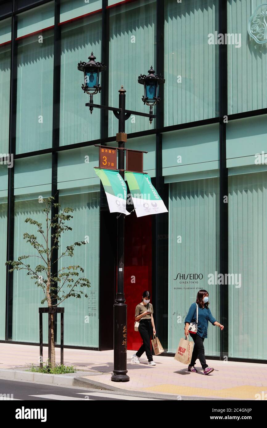 Menschen, die vor der Eröffnung am Shiseido Global Flagship Store im Ginza Building vorbeikommen. Tokyo Olympic Banner Hand von Lampenpfosten. (26. Juni 2020) Stockfoto
