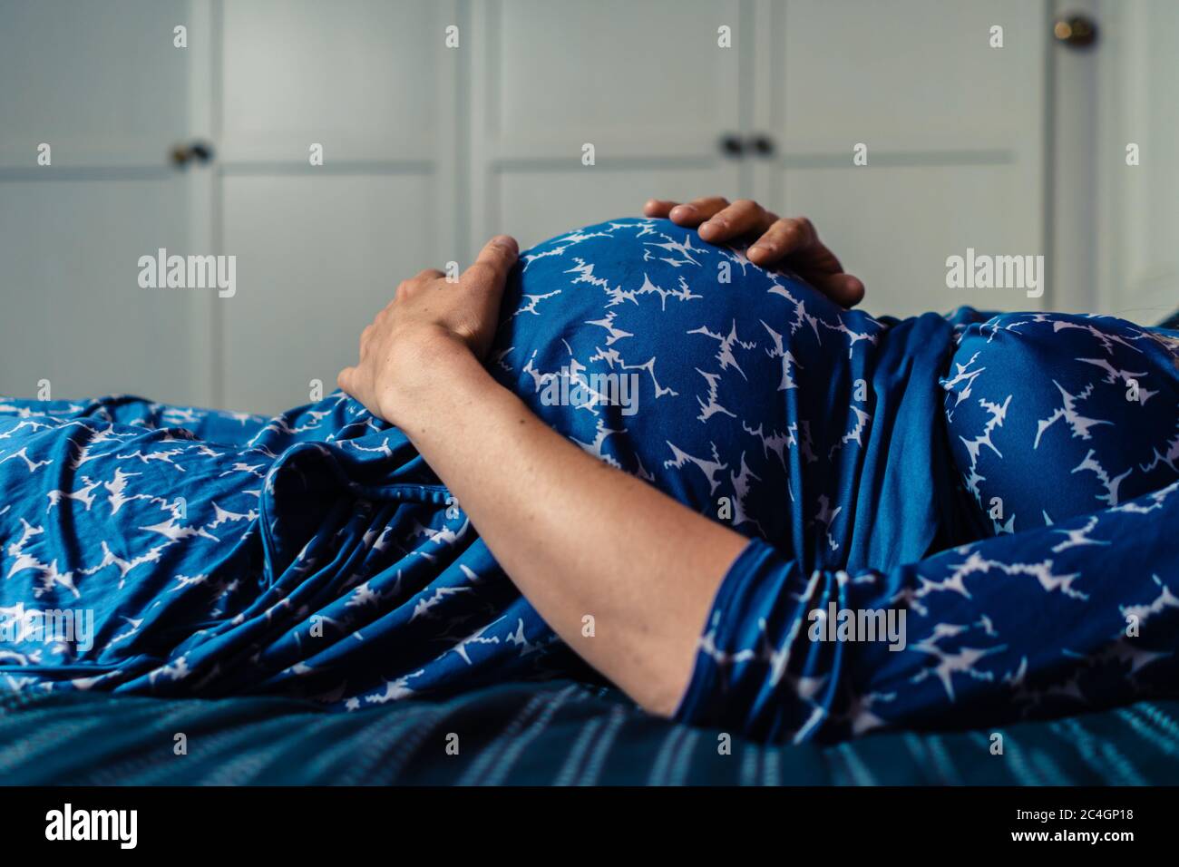 Eine schwangere Frau, die ein Nachthemd trägt, liegt auf einem Bett mit der Hand auf ihrem Bauch Stockfoto