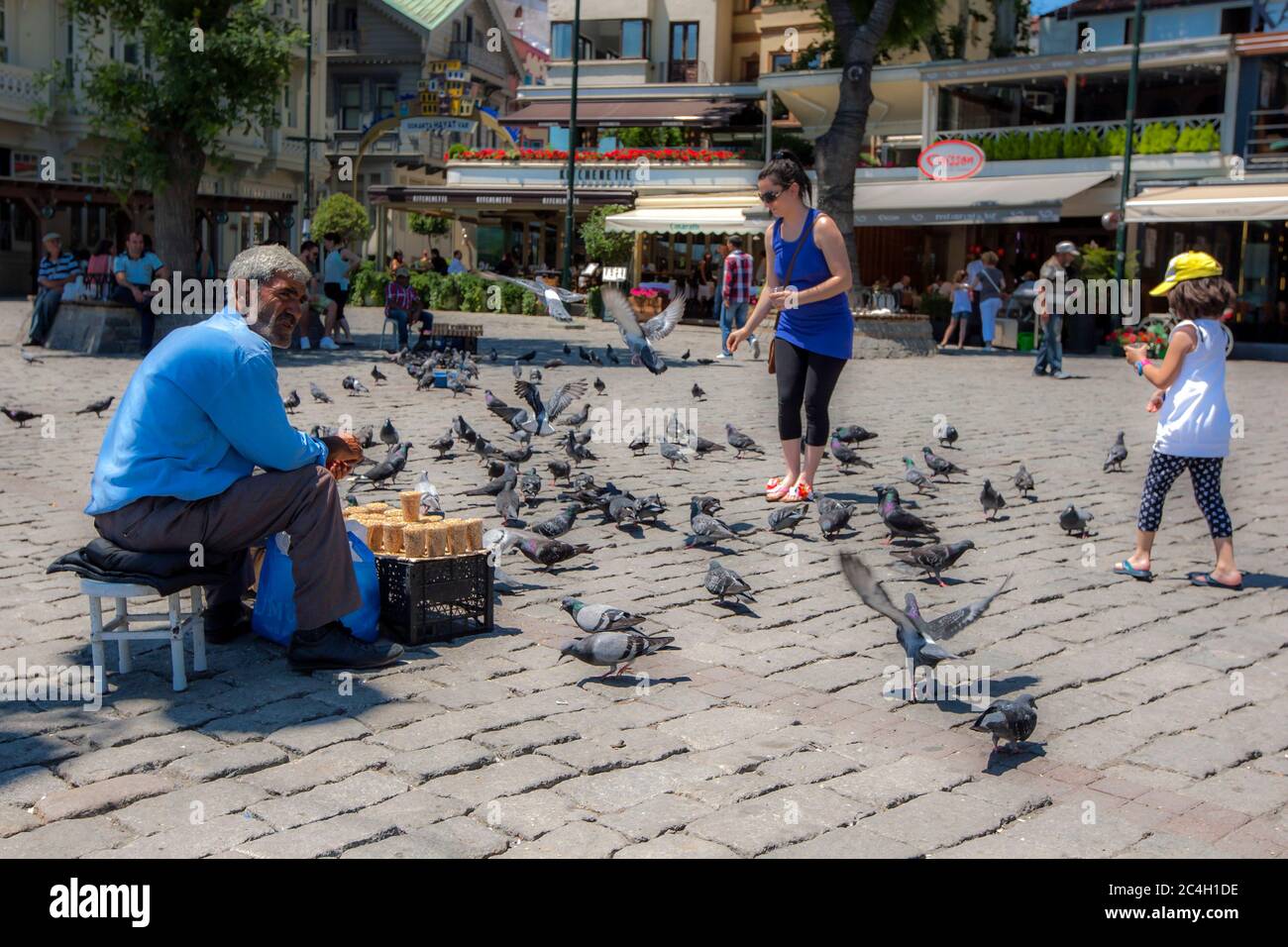 Ein Mann, der Weizenbecher verkauft, um die Tauben zu füttern, sitzt in einem Park neben dem Bosporus bei Ortakoy in Istanbul, Türkei. Stockfoto