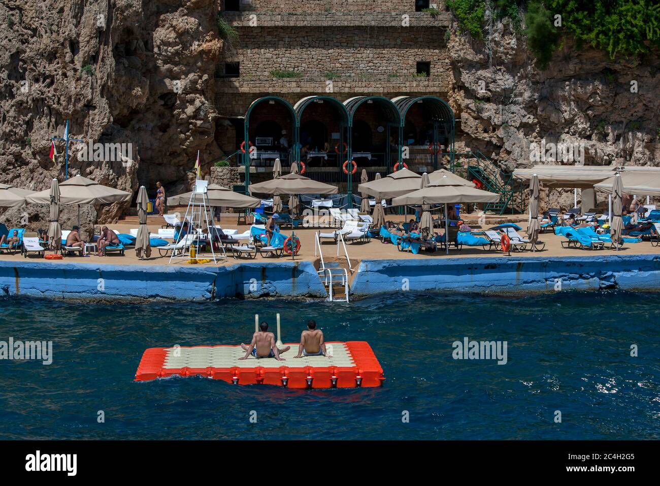 Touristen entspannen sich auf einer künstlichen Plattform am Fuße der Klippen unterhalb der Altstadt von Kaleici in der Bucht von Antalya in der Türkei gebaut. Stockfoto