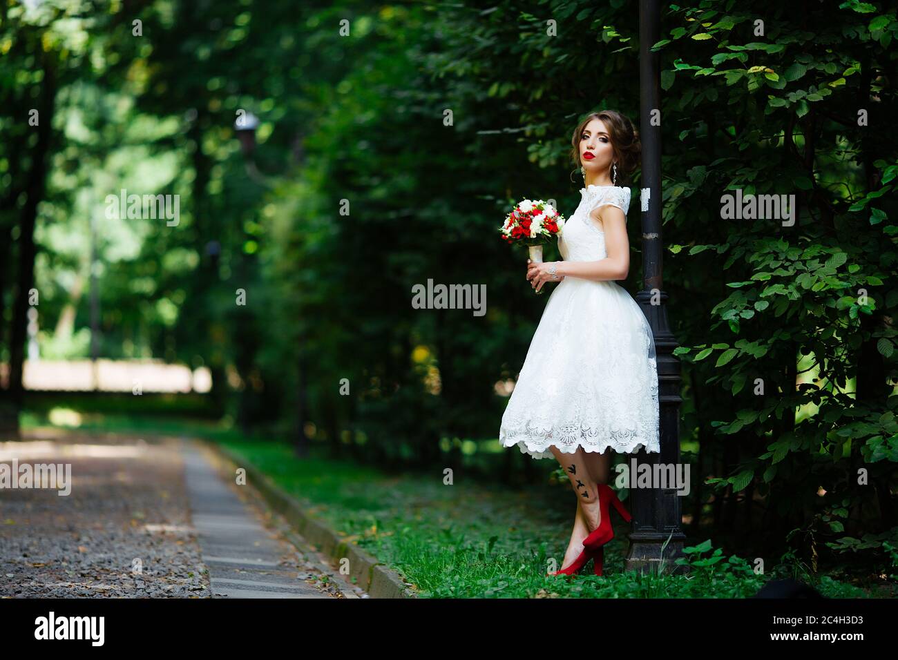 Brunette Braut in einem Kleid mit einem Brautstrauß im Park auf einem Hintergrund von Grün Stockfoto