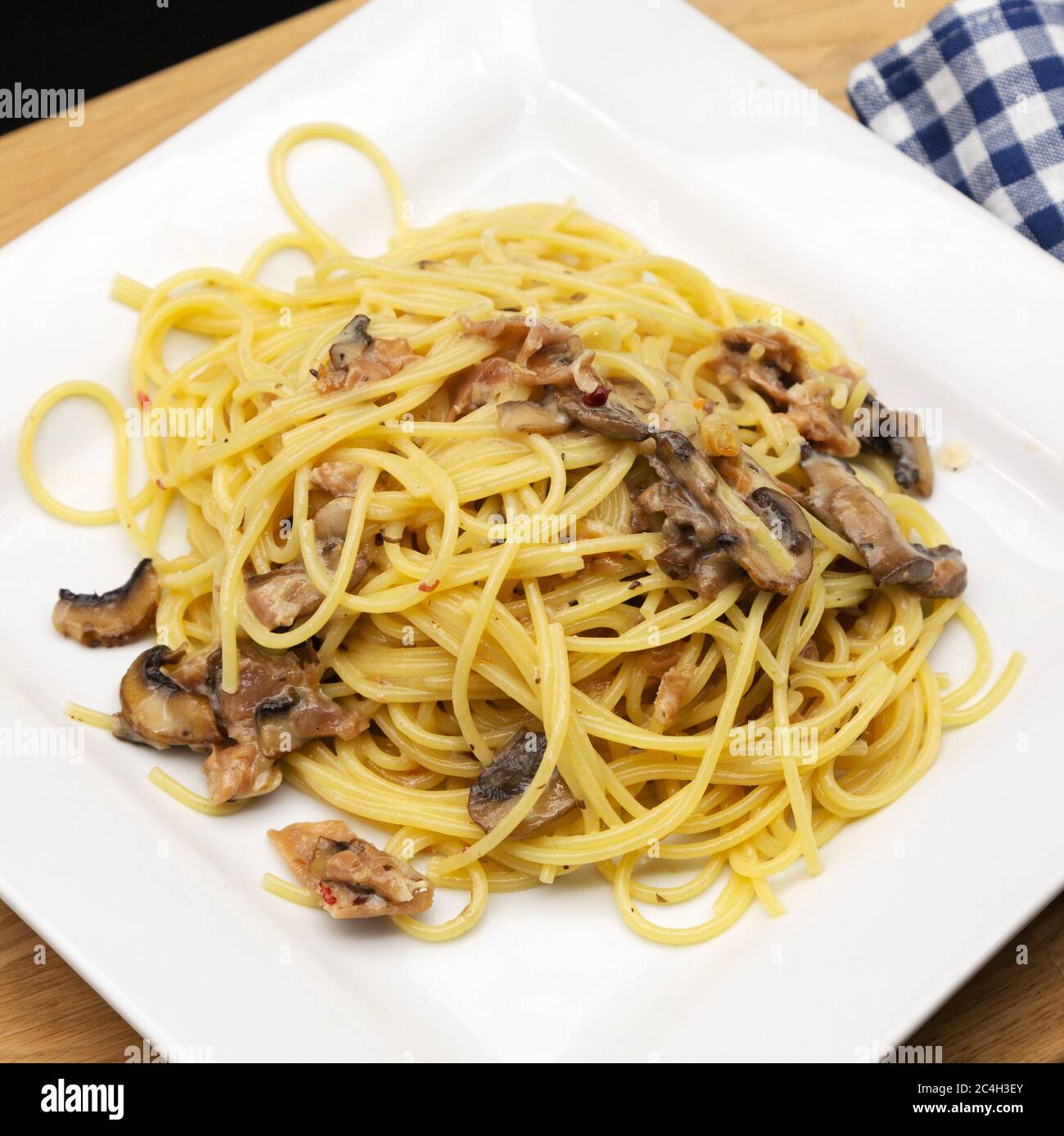 Spaghetti Carbonara, hergestellt mit Parmaschinken (Prosciutto di Parma) und Pilzen, präsentiert auf einem Holzbrett. Der Schinken wird rund um die Stadt Parm produziert Stockfoto