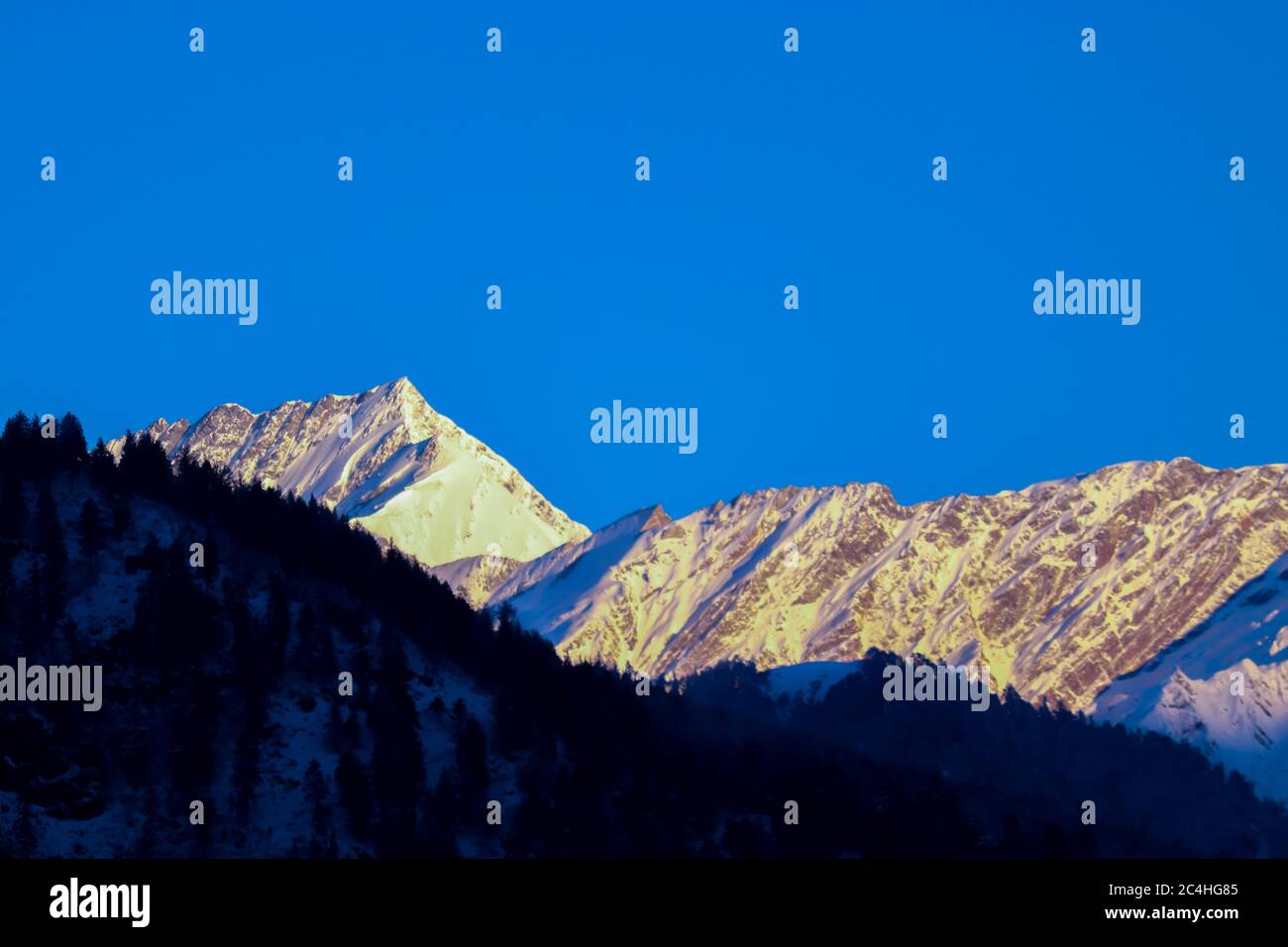 sonnenaufgang auf dem Gipfel eines schneebedeckten Berges. Der Berg vorne ist mit Pinien bedeckt. Fokus auf Unendlichkeit. Stockfoto