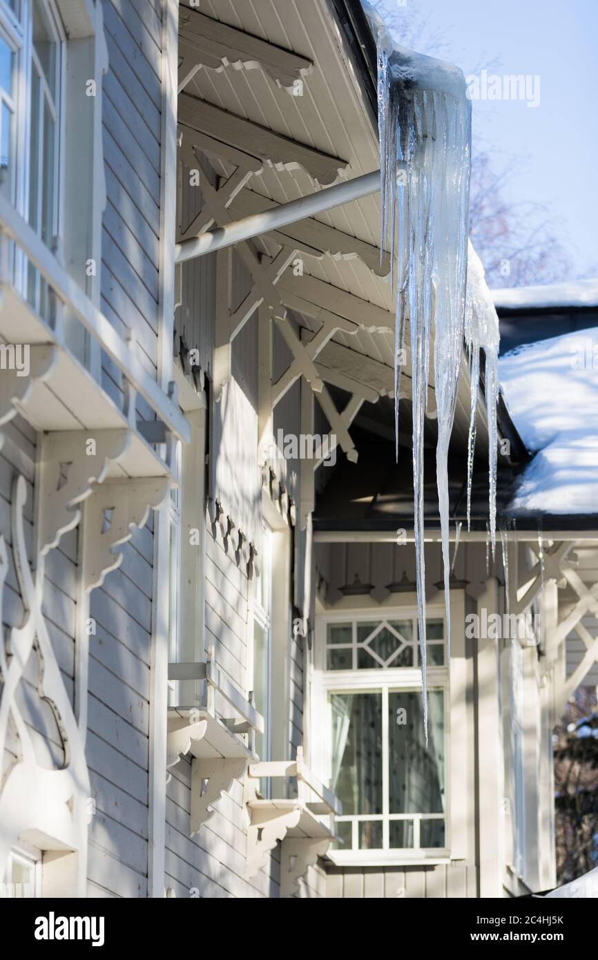 Eis Stalaktit hängen vom Dach mit Holzwand. Gebäude mit großen Eiszapfen bedeckt. Eiszapfen sind sehr gefährlich für das Leben. Schlechte thermische Isolierung Stockfoto