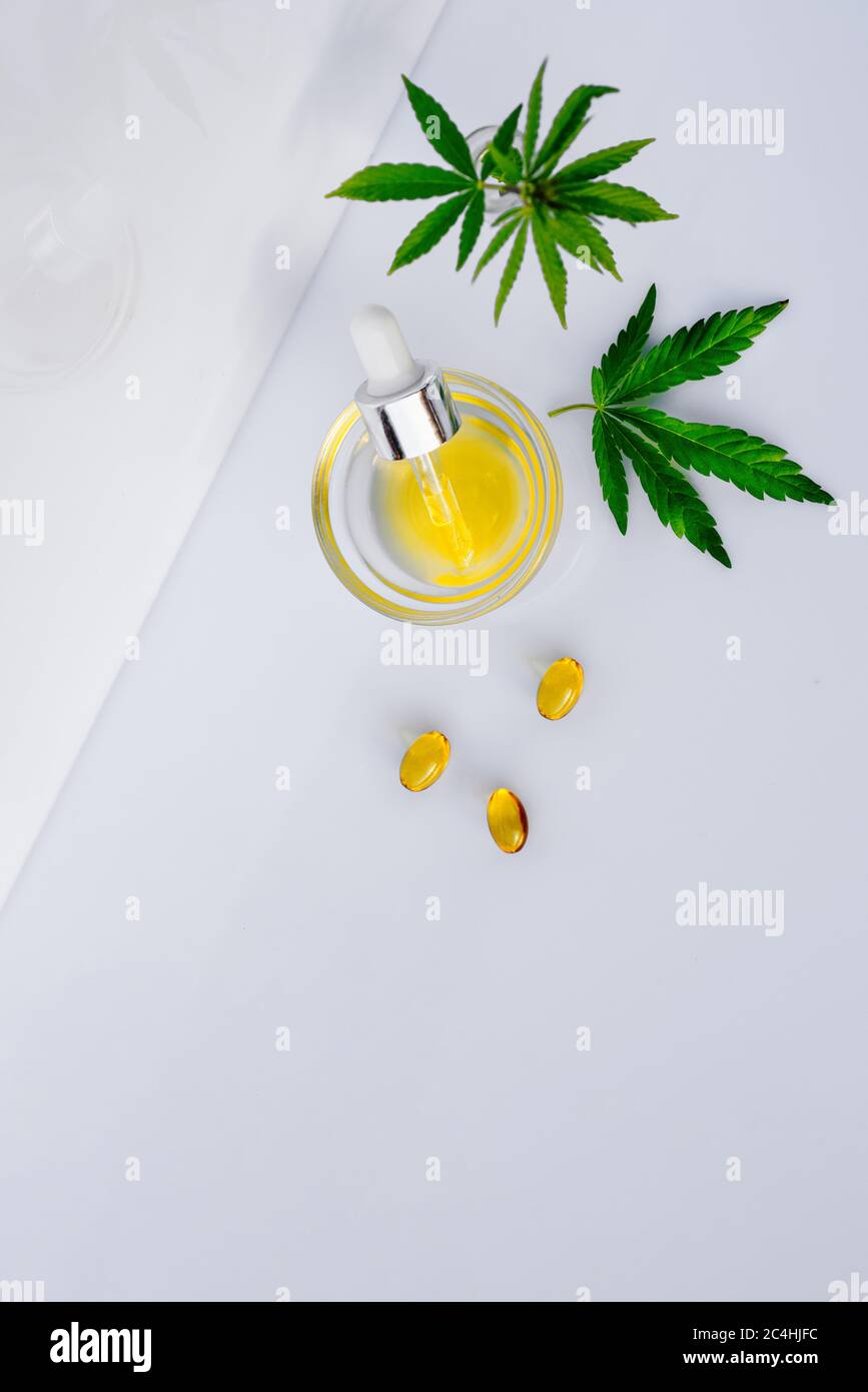 Pharmazeutisches CBD-Öl und Kapseln auf einem weißen Labortisch mit Cannabisblättern Stockfoto