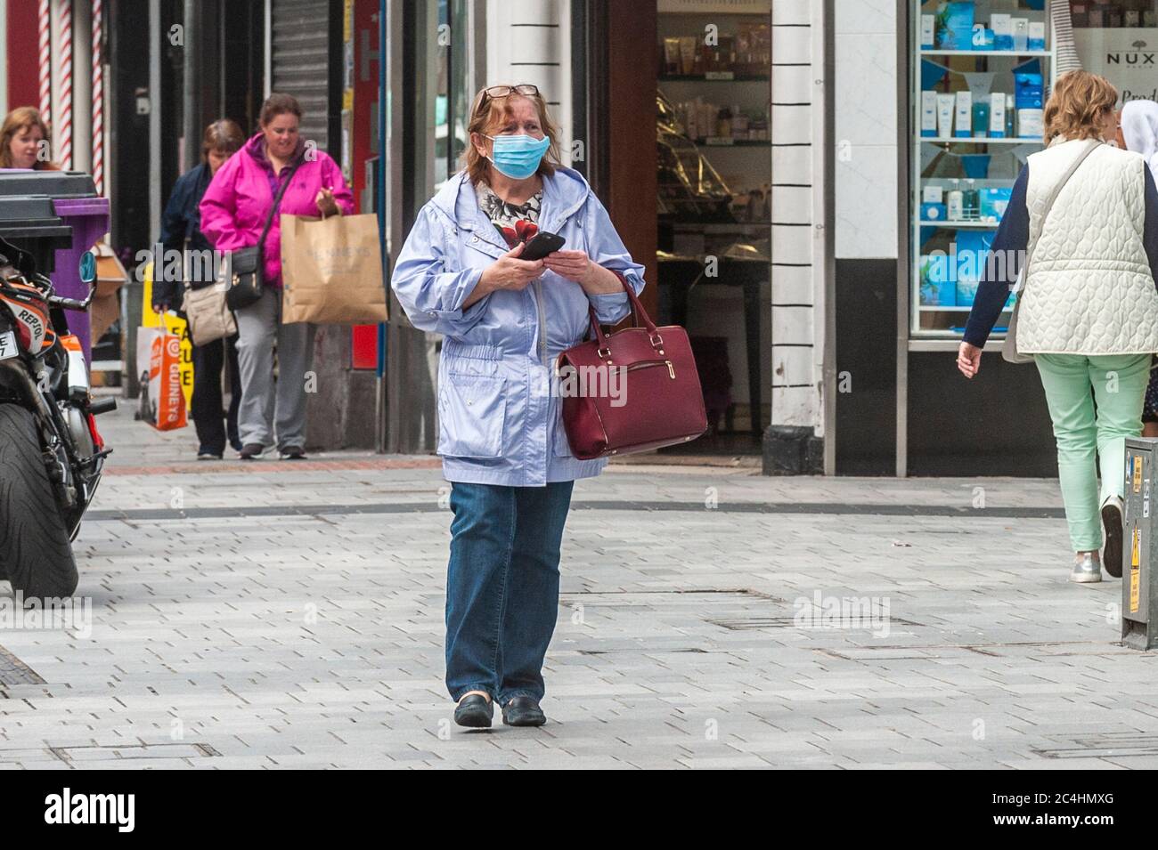 Cork, Irland. Juni 2020. Eine Frau geht in Cork Stadt mit einer Gesichtsmaske, um sich vor Covid-19 zu schützen. Die Regierung lockern am Montag, 29. Juni, weitere Einschränkungen des Coronavirus auf, sodass mehr Unternehmen wieder eröffnet werden können, darunter Friseure und Hotels. Quelle: AG News/Alamy Live News Stockfoto