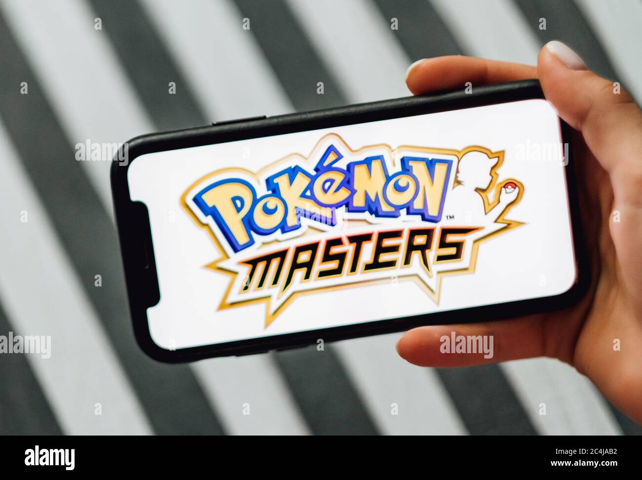 Hände halten iPhone mit Pokemon Masters auf dem Bildschirm. Stockfoto