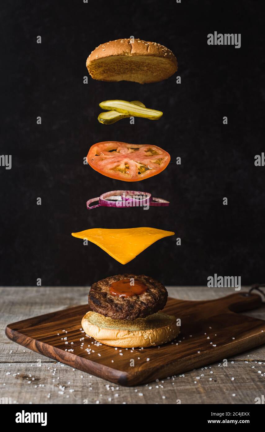 Burger mit schwebenden Zutaten auf schwarzem Hintergrund. Stockfoto
