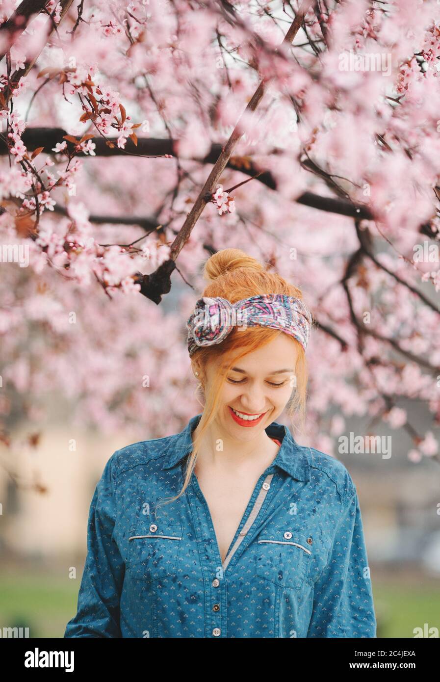 Junge Frau, die im Regen unter der Frühlingsblüte steht Baum Stockfoto