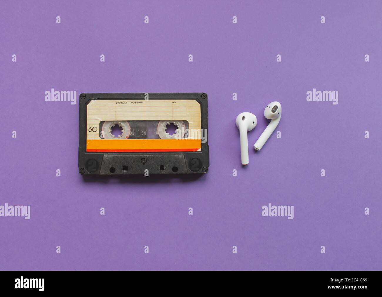 Draufsicht auf einen kabellosen Kopfhörer und eine Audiokassette auf dem violetten Hintergrund. Konzept der Entwicklung der Musik. Stockfoto