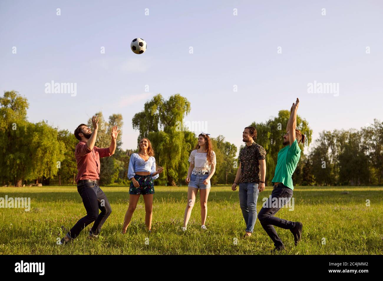 Gruppe von Freunden, die Spaß mit einem Ball auf einem Gras Picknick in einem Sommerpark spielen. Stockfoto