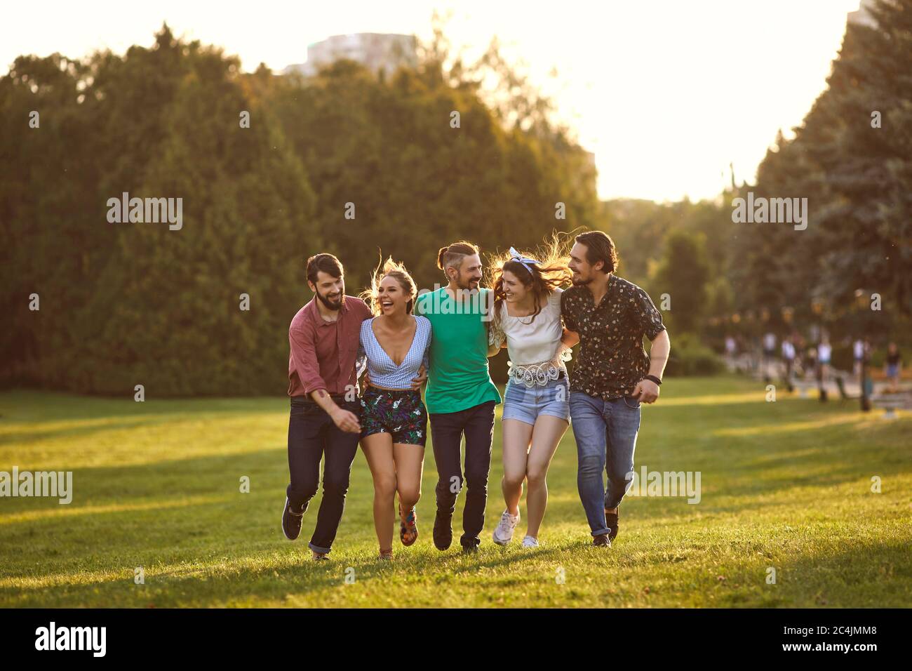 Eine Gruppe junger Leute haben Spaß, sich in einem Sommerpark entlang des Grases zu umarmen. Stockfoto