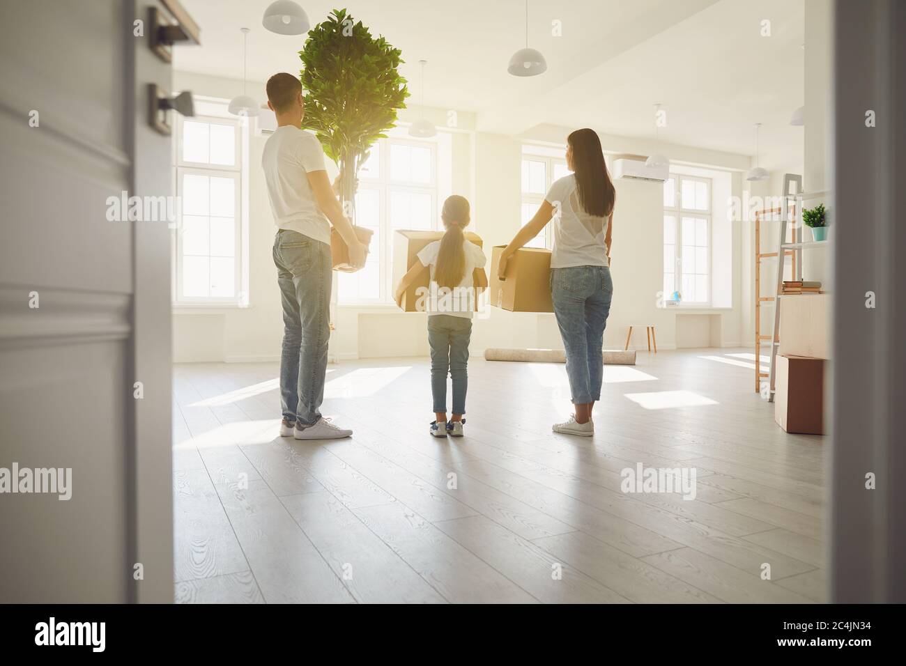 Glückliche Familie mit Kindern, die in einem neuen Mehrfamilienhaus mit Kisten umziehen. Rückansicht. Stockfoto