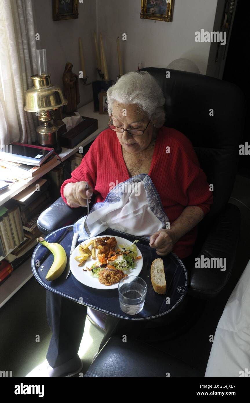 Ältere Dame auf dem Sessel sitzend, auf dem Tablett essend Stockfoto