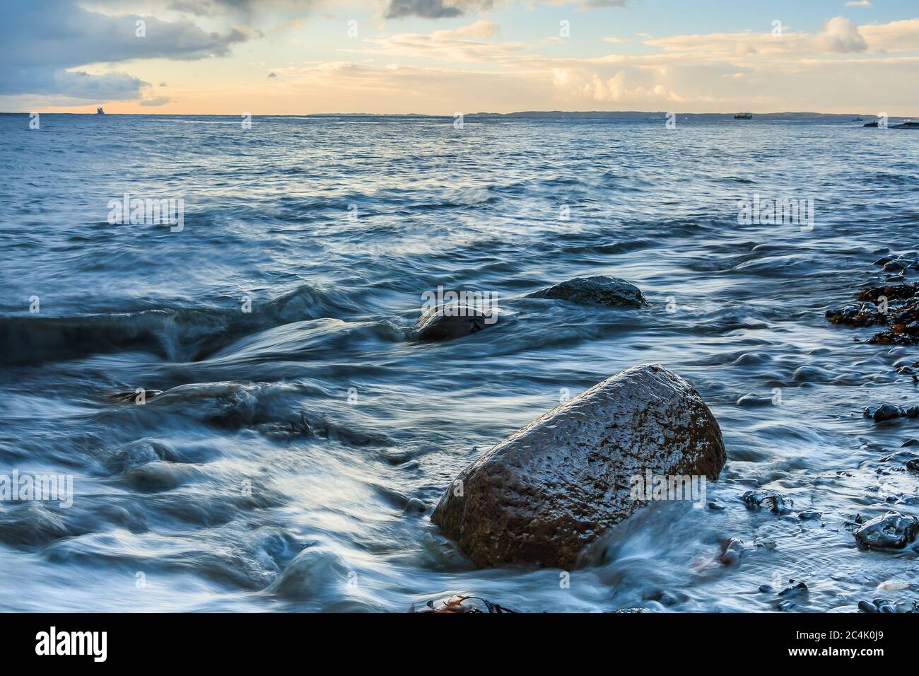 Küstenabschnitt an der Ostsee am Morgen bei Sonnenaufgang. Heller Anschwellen mit blauem Himmel auf der Insel Rügen. Großer Stein im Vordergrund Stockfoto