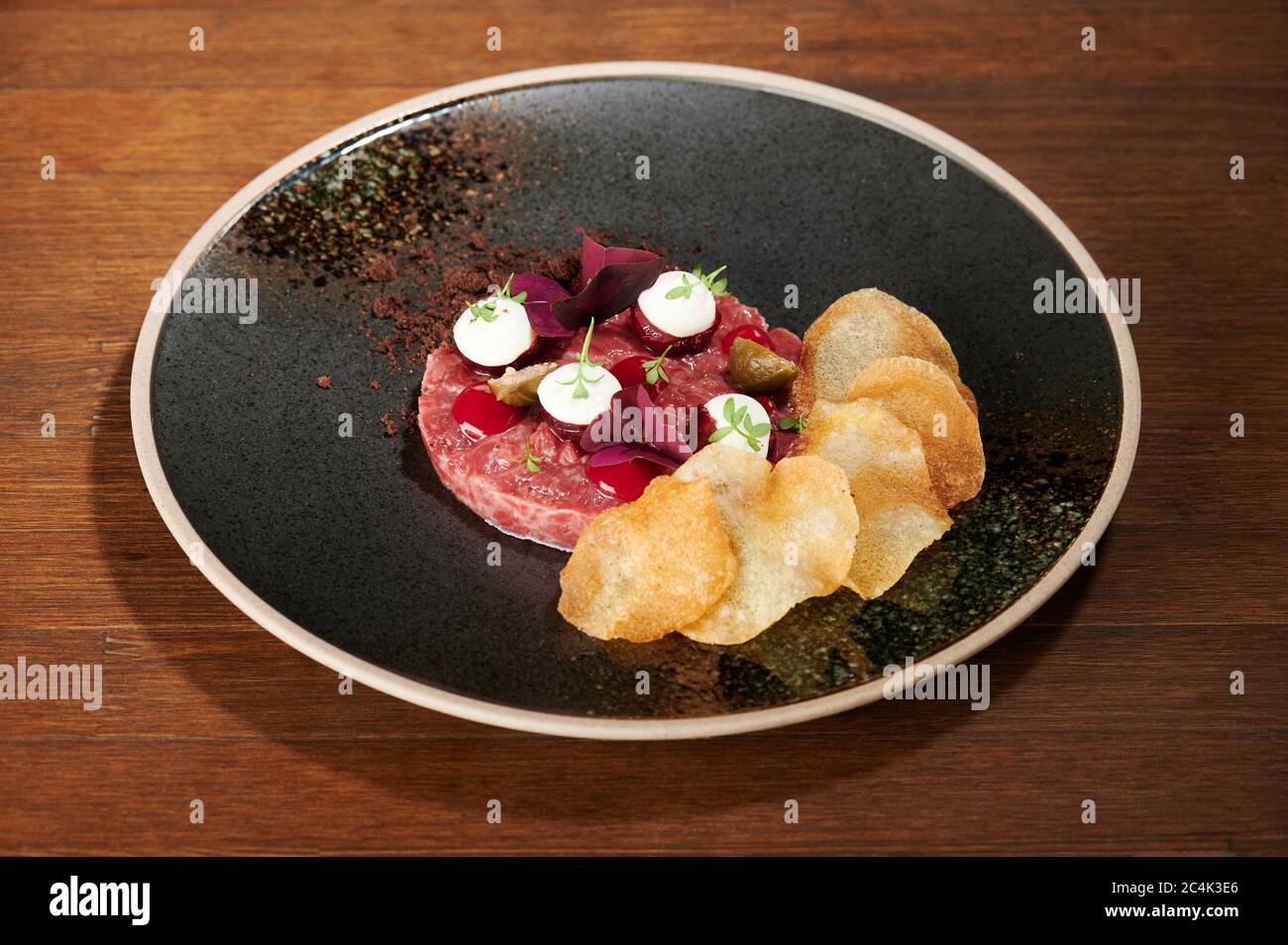 Frisches Tartarmenü auf schwarzem grungigen Teller, Blick auf Holztisch Stockfoto