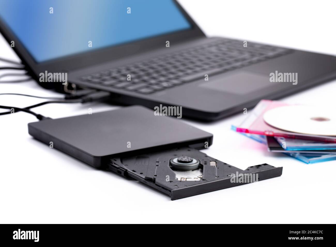 n Öffnen Sie das DVD-CD-Laufwerk des externen Computers mit einer Ansammlung von CD-Hüllen und einem Notebook im Hintergrund Stockfoto