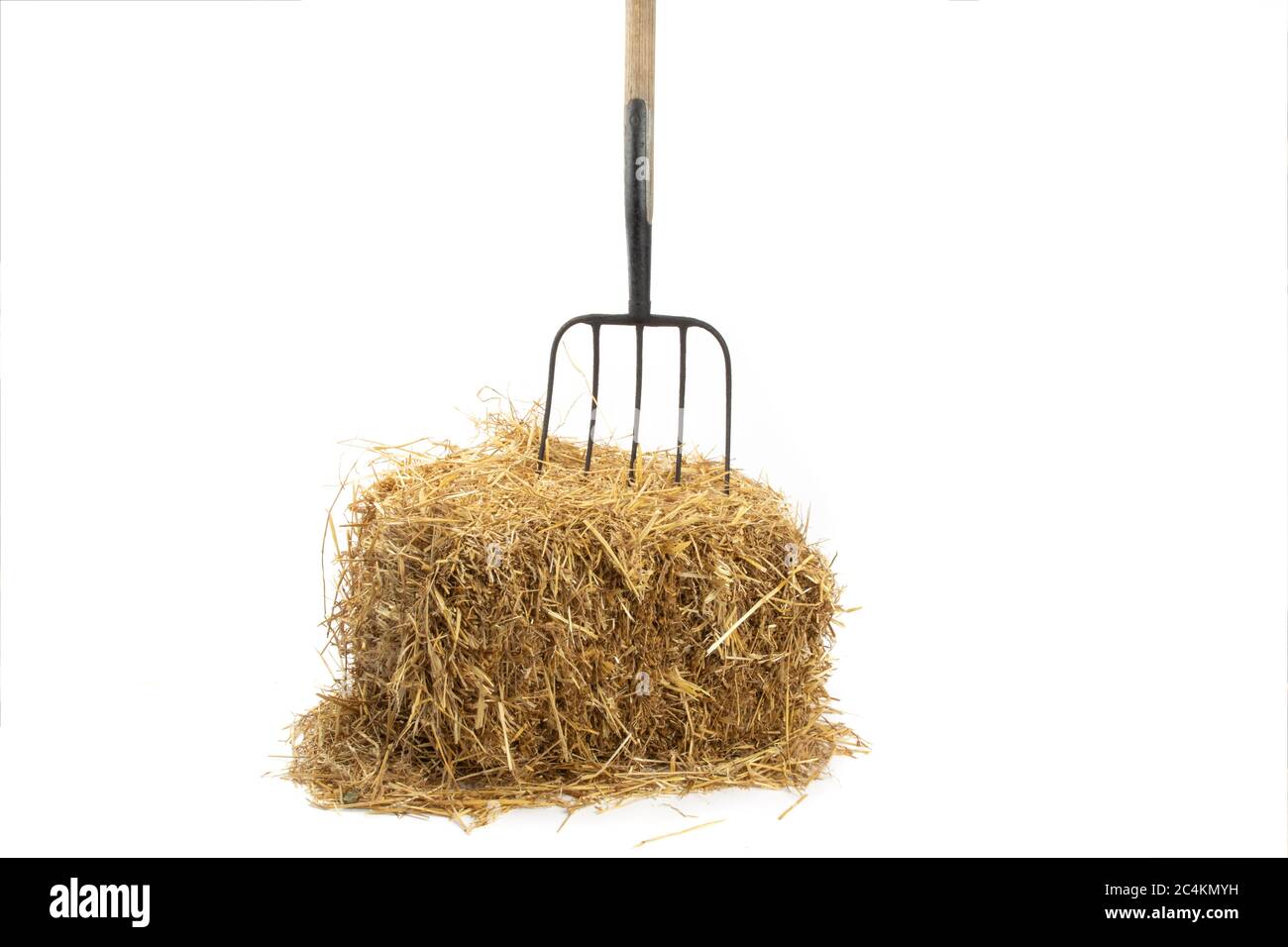 Eine alte Pitchgabel, die in einem Strohballen auf Weiß isoliert stecken bleibt Stockfoto