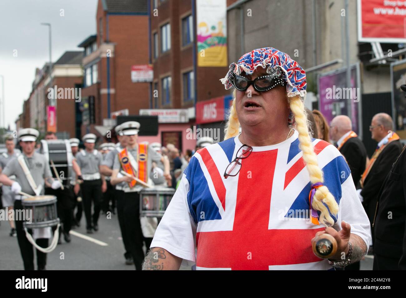 Ein Mann mit einer blonden Perücke und einem Union Jack T-Shirt bei der Parade am 12. (12.) Juli in Belfast. Stockfoto