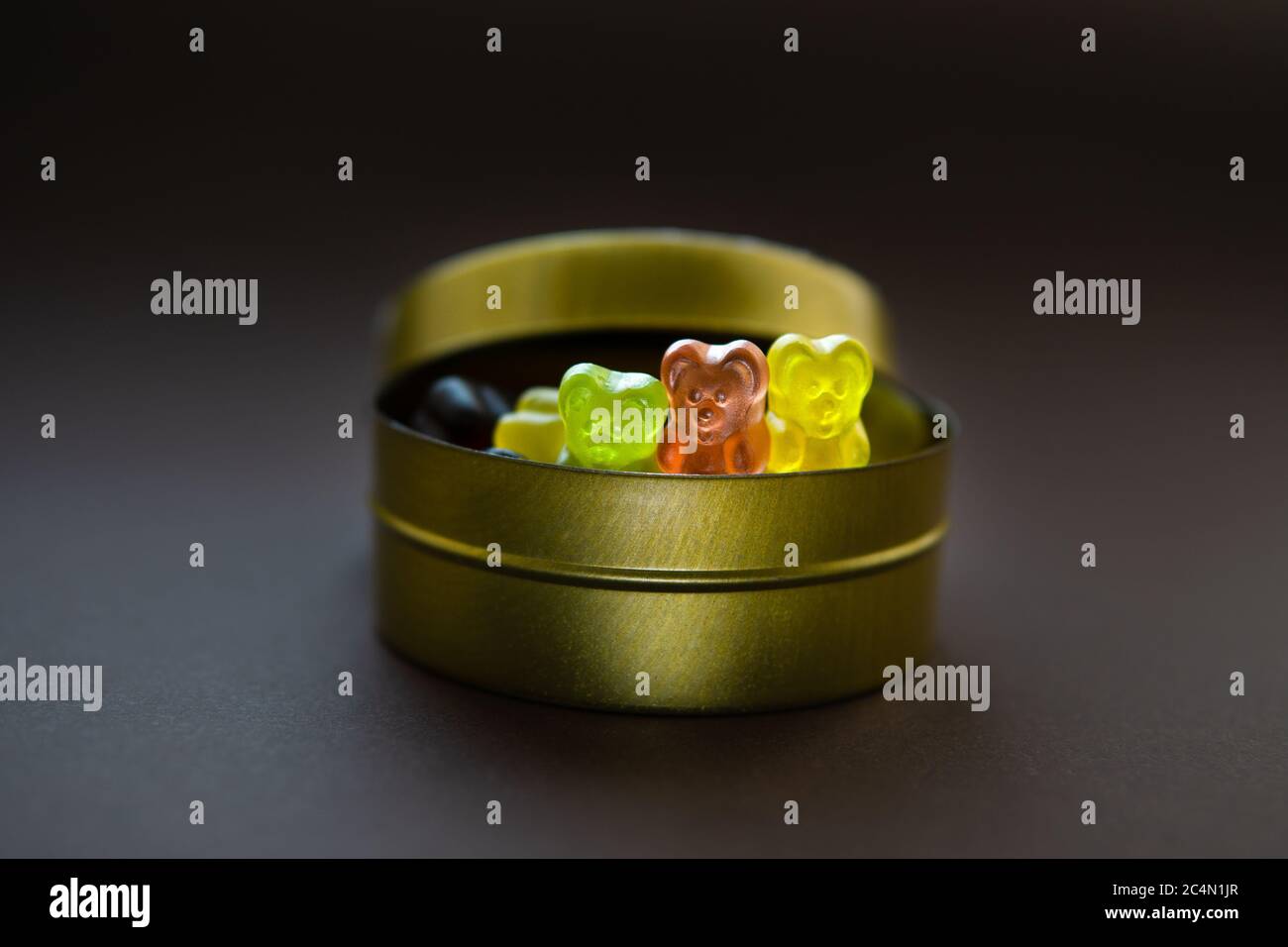 Nahaufnahme von drei Gelee-Bären, die aus einer runden Dose Bonbon-Box auf braunem Hintergrund gucken. Selektiver Fokus. Stockfoto