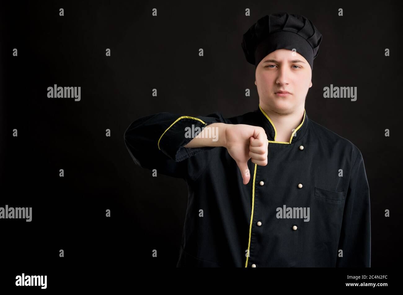 Portrait von jungen Mann in einem schwarzen Koch Anzug gekleidet zeigt Abneigung posiert auf einem schwarzen isolierten Hintergrund mit Kopie Raum Werbefläche Stockfoto