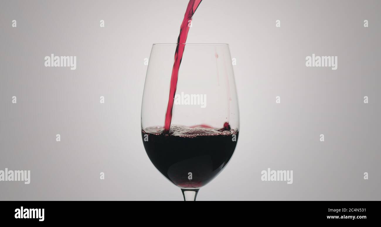 Rotwein gießen in Weinglas auf neutralem Hintergrund Stockfoto