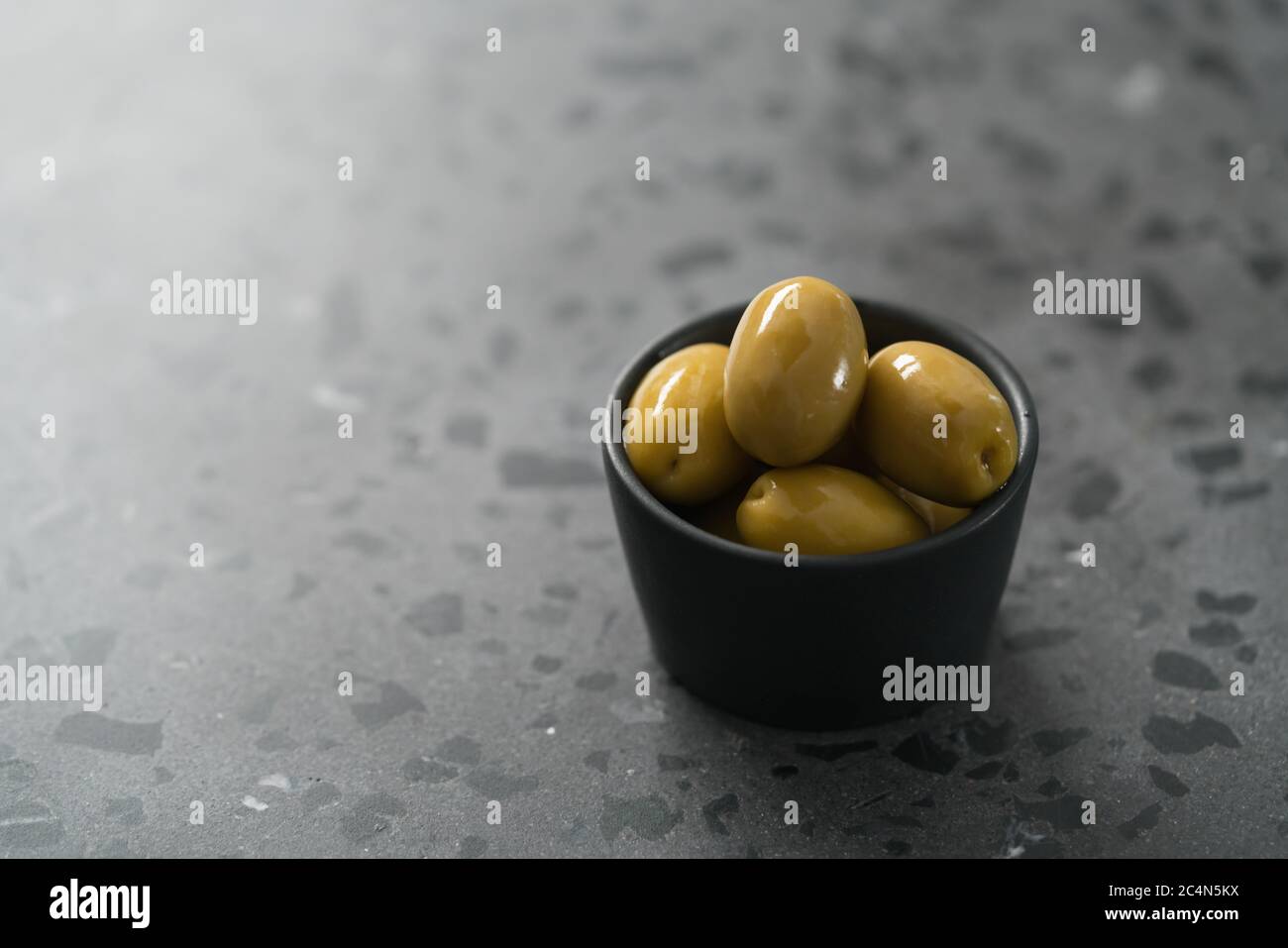 Ganze große grüne Oliven in kleiner schwarzer Schale auf Beton Hintergrund Stockfoto