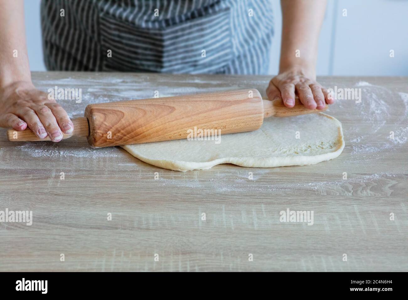 Den Hefeteig mit einer Holztrommel ausrollen Stockfoto