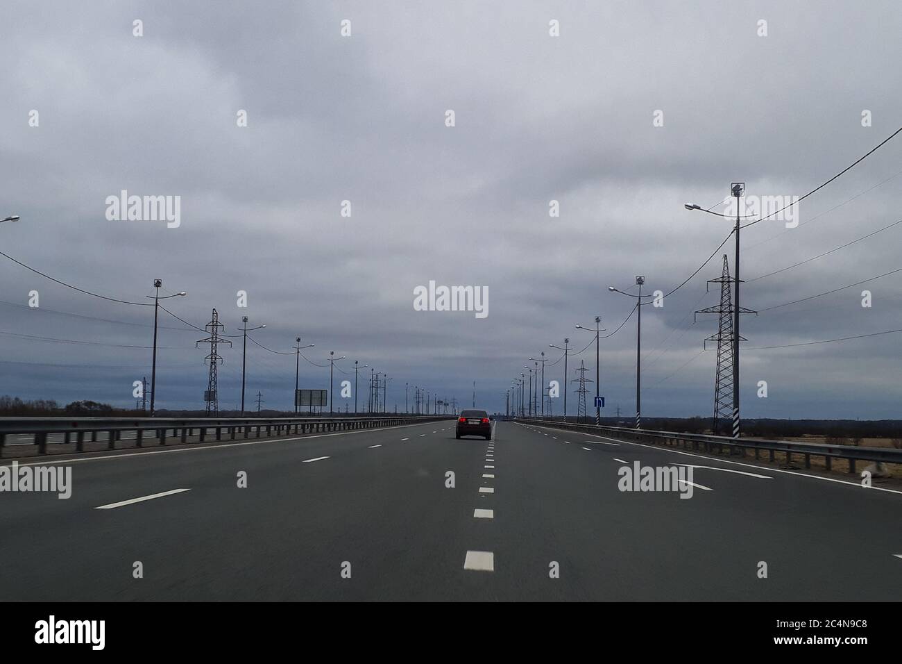 Eine Straße oder eine Autobahn, die Autobahn erstreckt sich bis zum Horizont. Blick vom Fenster des Autos. Reise, der Weg nach Hause. Kalte nördliche Natur, Sommer, grau bewölkt niedrigen Himmel. Stockfoto