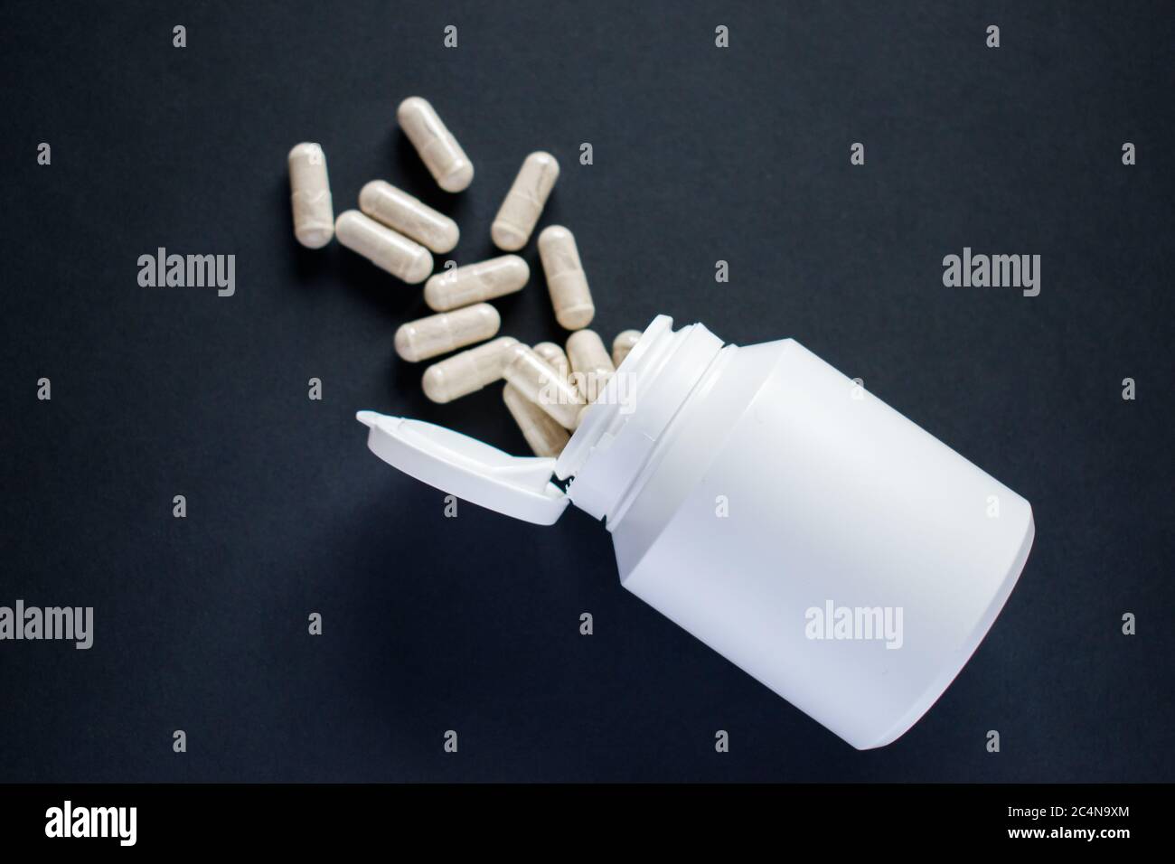 Verschüttete medizinische Pillen aus der weißen Pille Flasche auf schwarzem Hintergrund Stockfoto