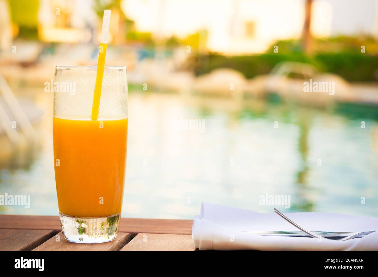 Sonnige Nahaufnahme eines Glases frischen Mangosaftes, der auf einem Tisch in der Nähe des Pools steht Stockfoto