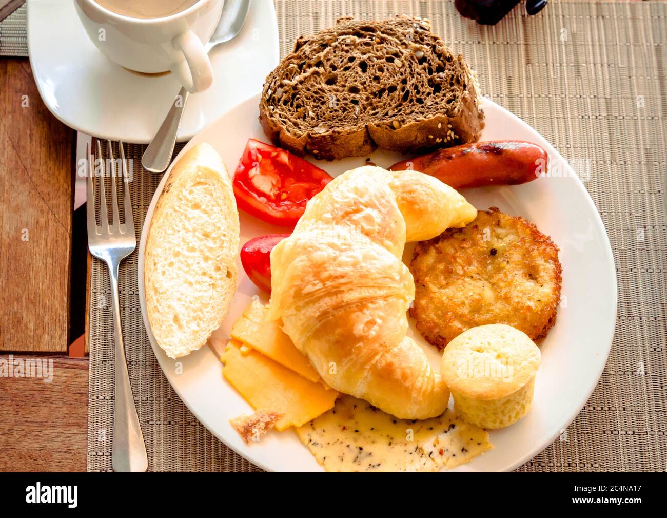 Frühstück im Café mit einer Tasse Kaffee und Croissant, Brot, Käse, Tomaten auf dem Teller. Stockfoto