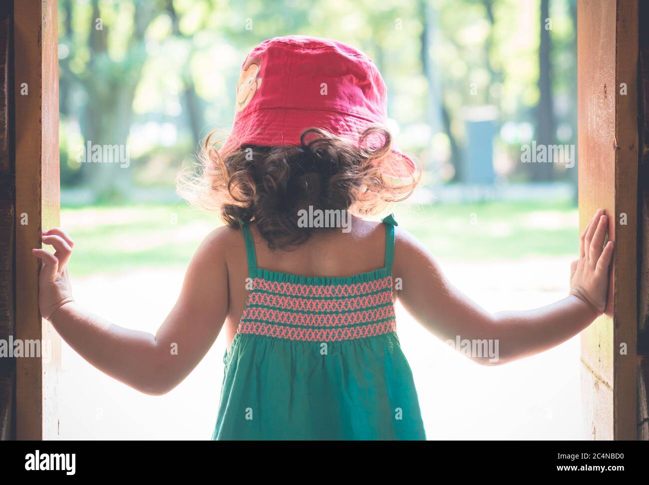 Kleines Mädchen in rotem Hut steht in der Tür. Sonniger Sommertag. Stockfoto