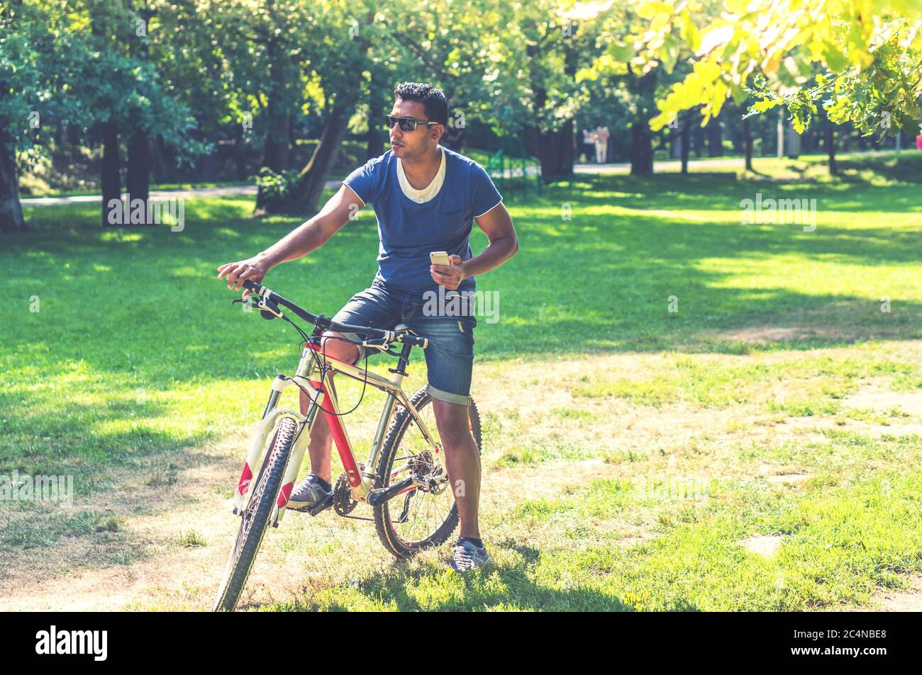 Junger Inder auf dem Fahrrad mit seinem Smartphone im Park Stockfoto