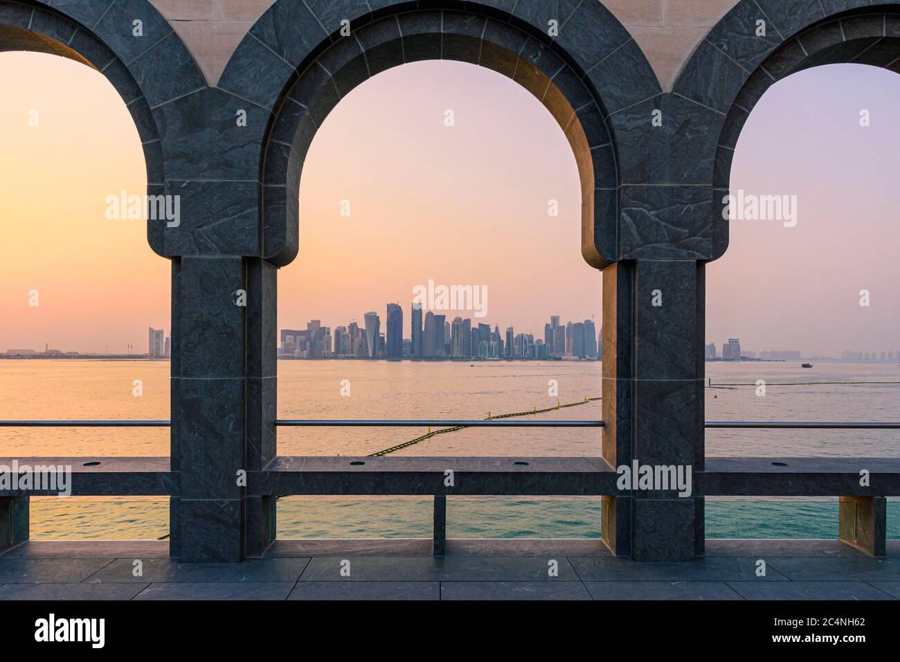 Blick auf die Skyline von Doha bei Sonnenuntergang durch die Bögen des Innenhofs im Museum für Islamische Kunst, Doha, Katar Stockfoto